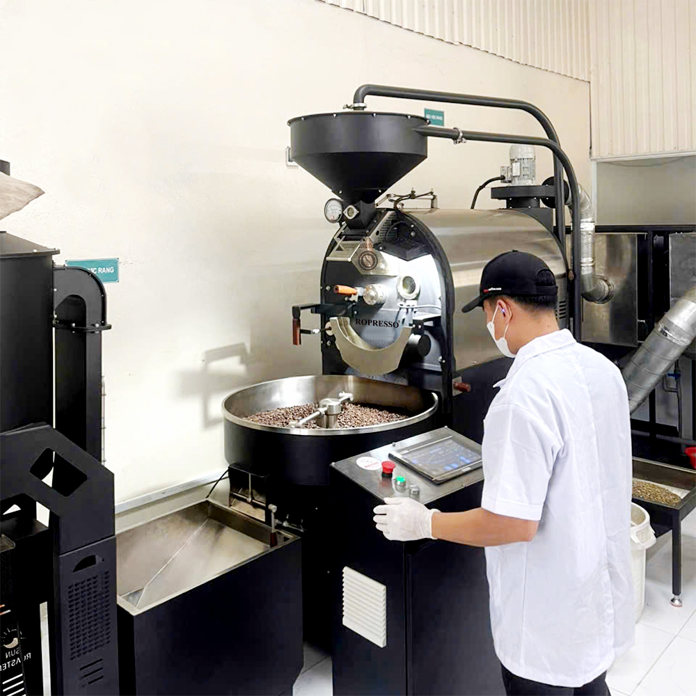 Người vận hành theo dõi máy rang và quan sát mẫu hạt cà phê bằng que lấy mẫu.